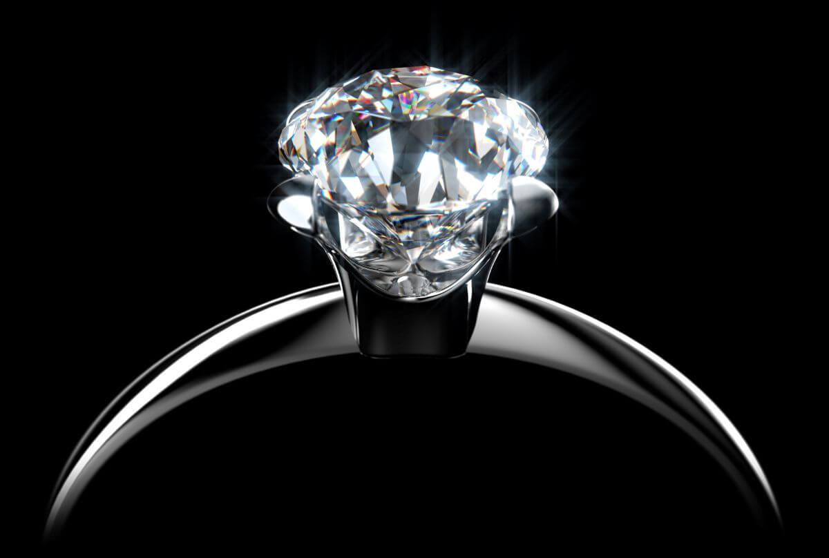 Single diamond engagement ring with a large round stone on a polished metal band against a black background