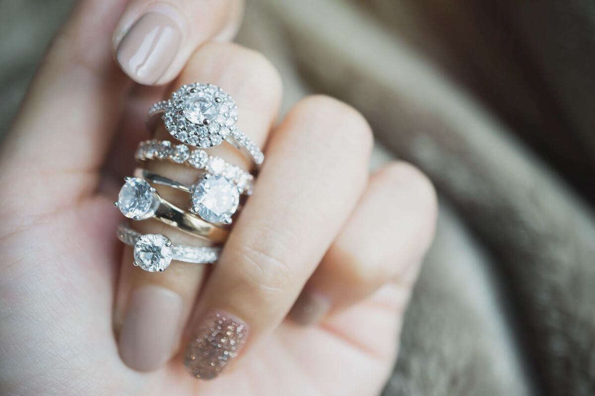 Hand wearing a stack of different diamond engagement rings and bands in various styles and settings