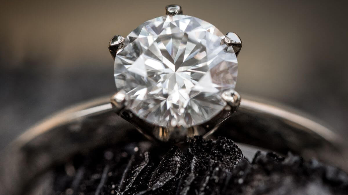 Close-up of a round brilliant diamond engagement ring in a six-prong white gold setting on a dark textured background